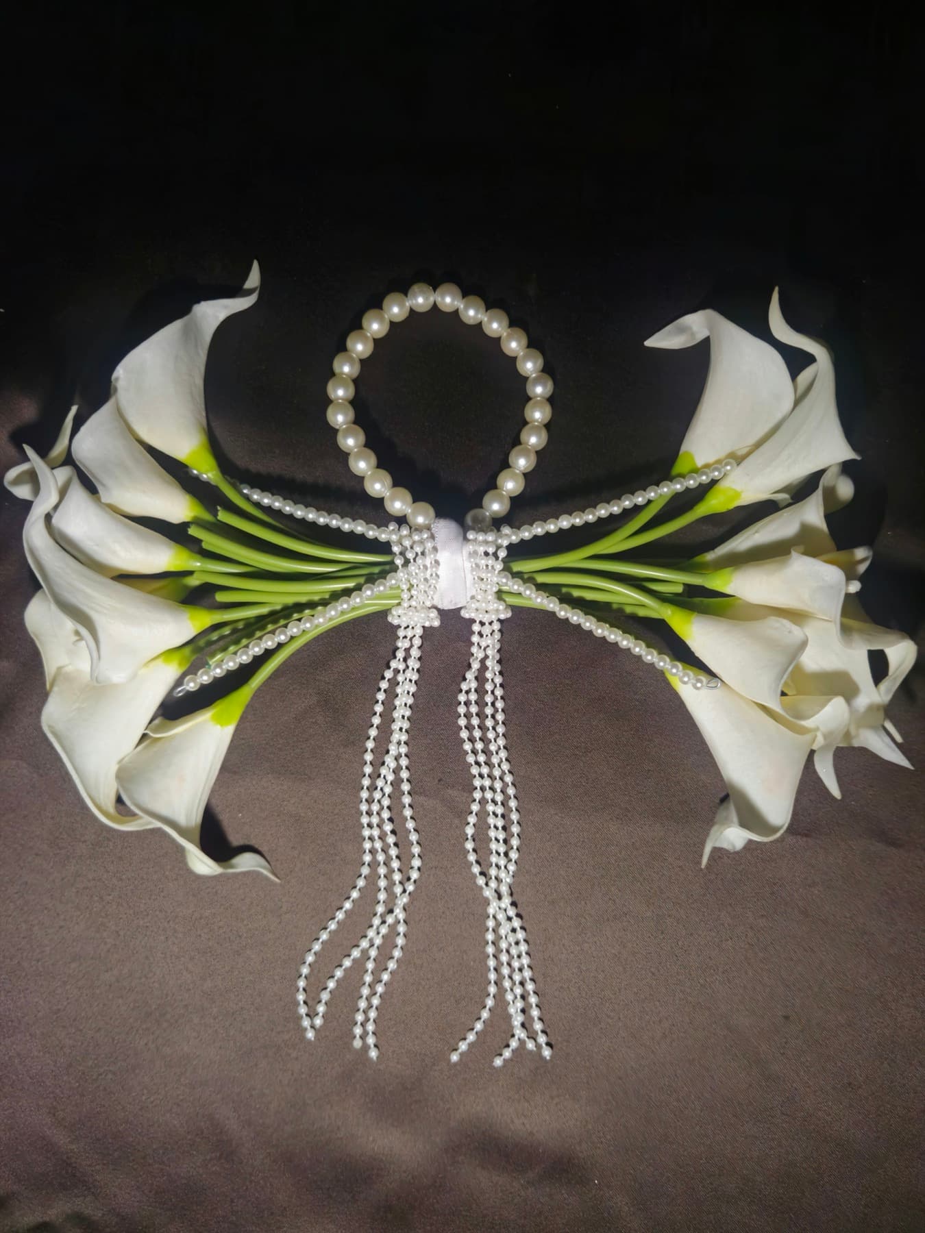 Ivory calla lilies and pearl strands arranged on dark satin
