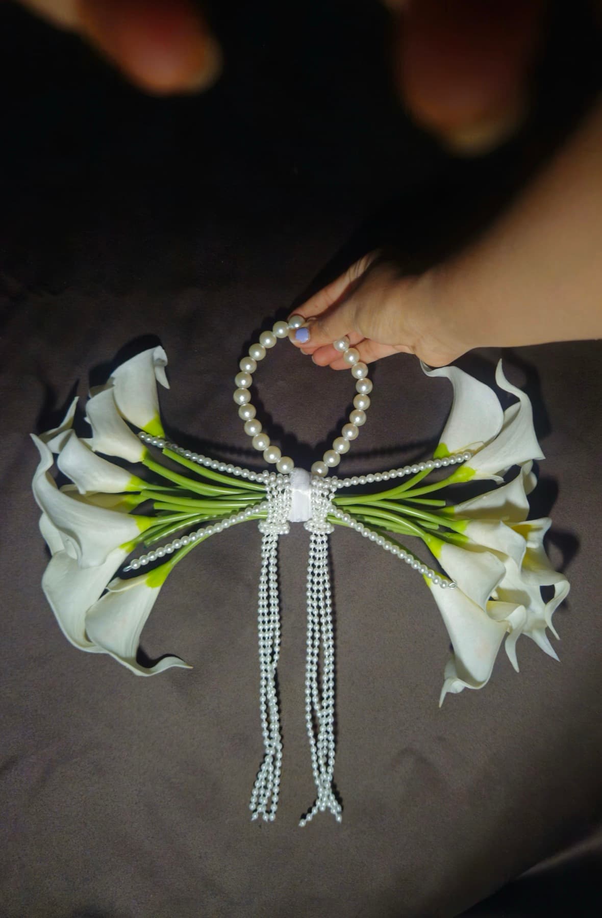 Ivory calla lily purse bouquet with cascading pearl strands on dark satin